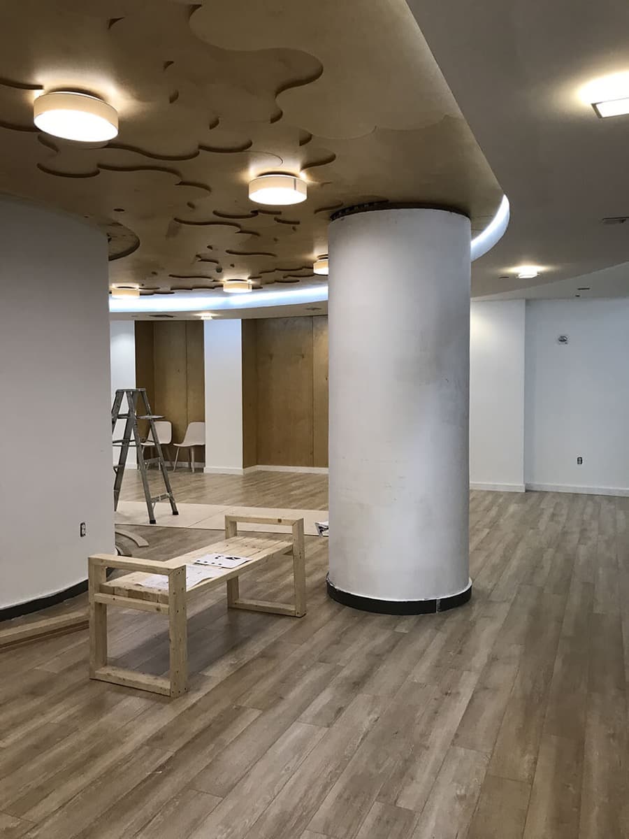 Open lobby with a round white column, wood-look flooring and a sculpted painted ceiling